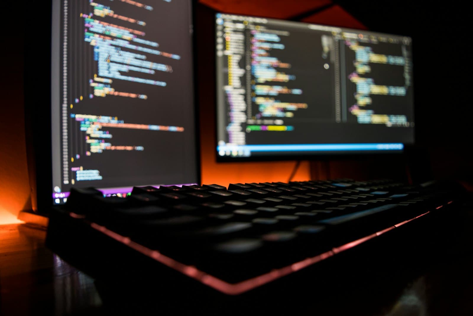 Beleuchtete Tastatur vor zwei Bildschirmen mit Code