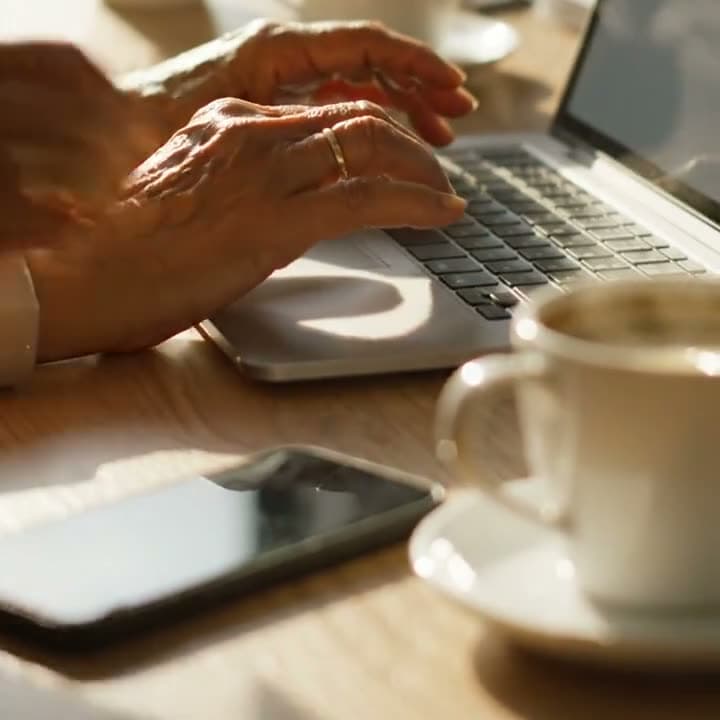 Hände tippen auf einer Laptop-Tastatur, daneben eine Tasse Kaffee